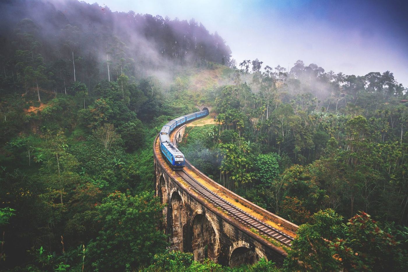 A train curving across Nine Arch Bridge in the morning mist